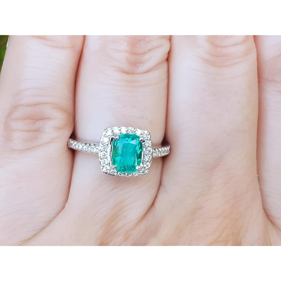 Women's cushion cut emerald ring with diamond halo and band in 14K white gold.