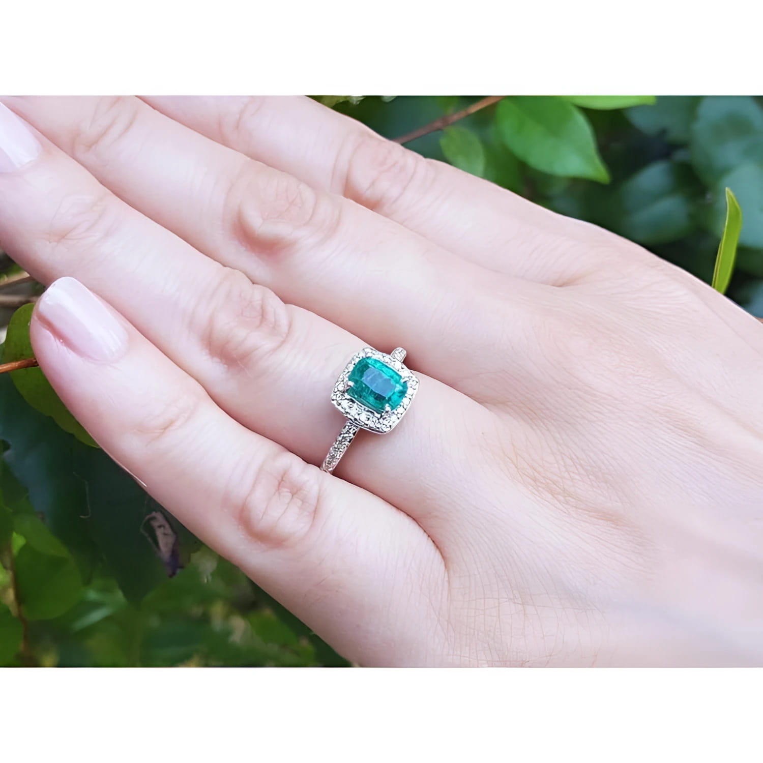 Women's 14K white gold ring with a cushion-cut emerald and diamond halo, worn on a hand.