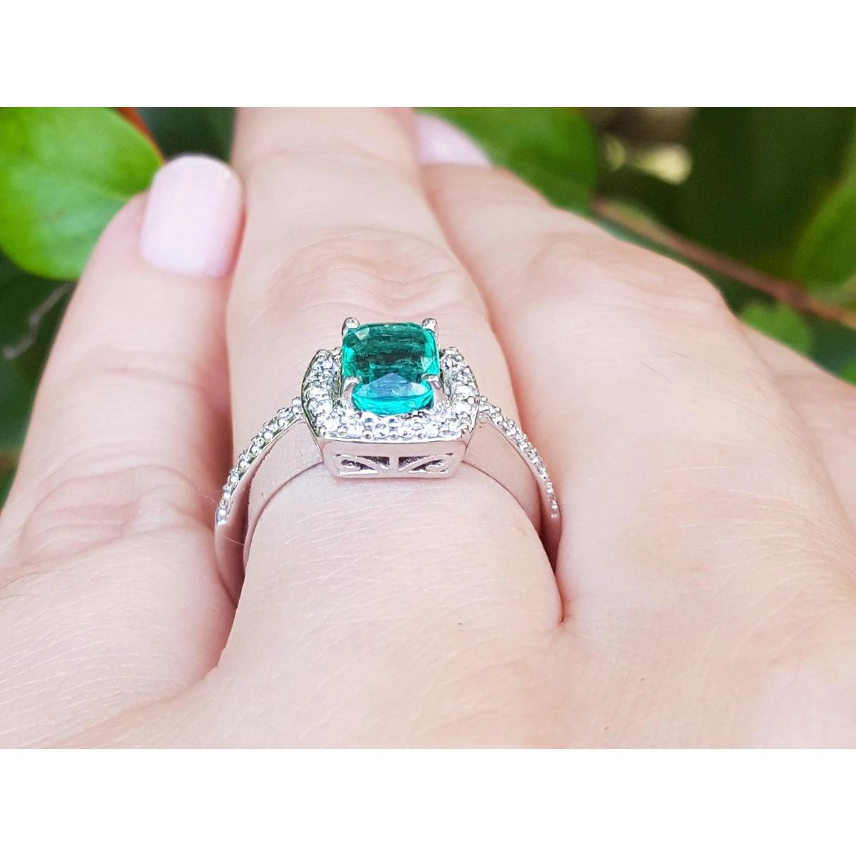 Natural emerald rings for women with diamond accents on a finger against a blurred green background.