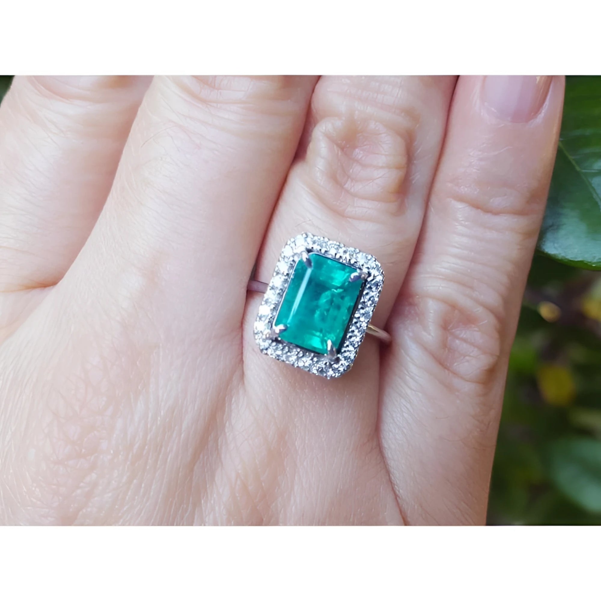 A colombian emerald ring for women adorned with a halo diamond on a person's finger.