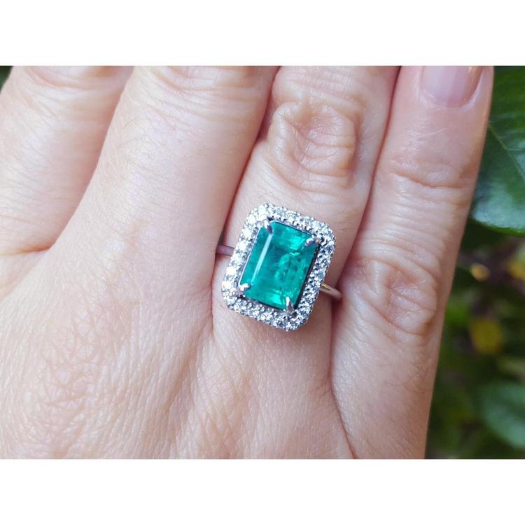 A colombian emerald ring for women adorned with a halo diamond on a person's finger.