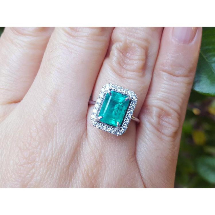 A colombian emerald ring for women adorned with a halo diamond on a person's finger.