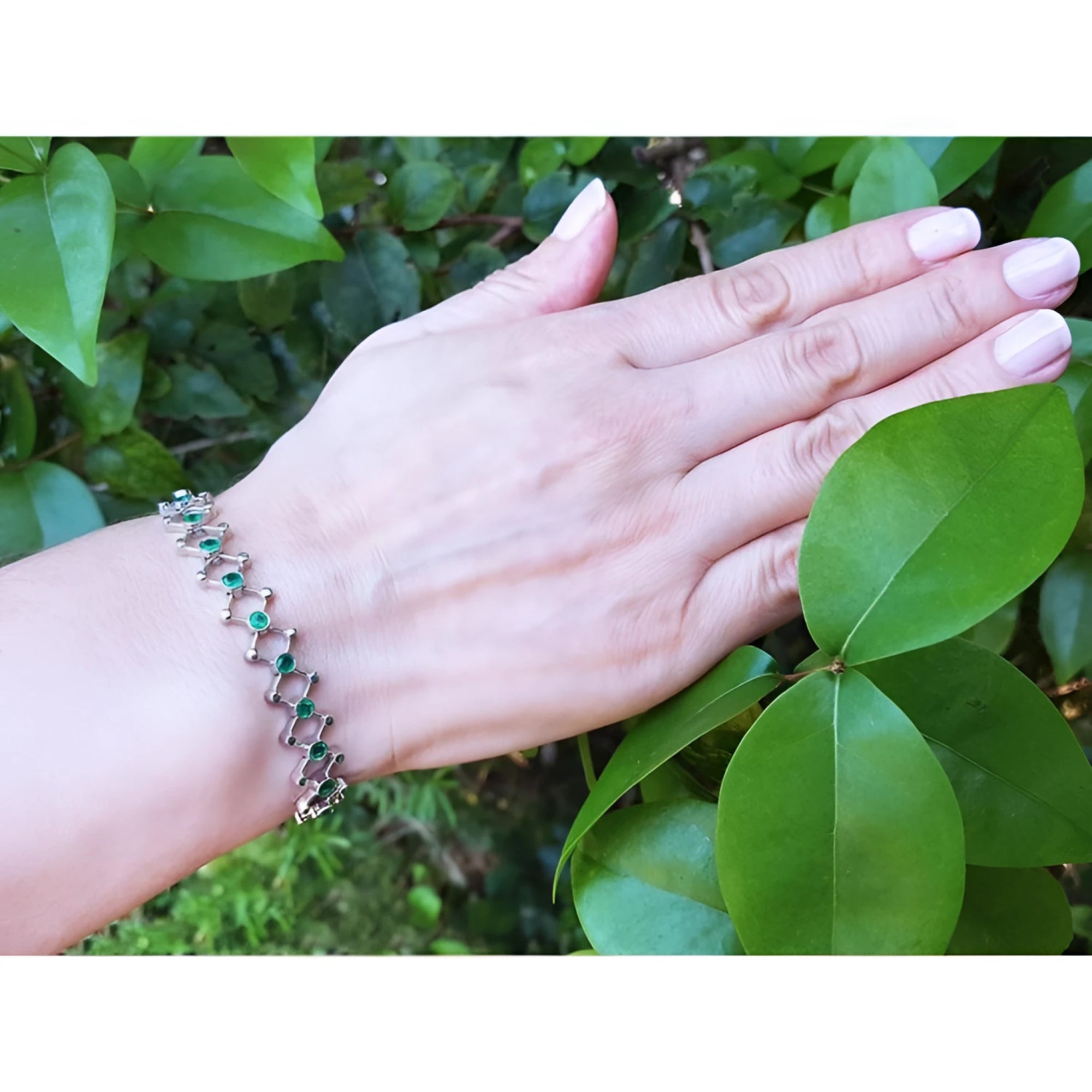 14K white gold bracelet with round Colombian emeralds bezel-set in diamond-shaped links on a woman's wrist.