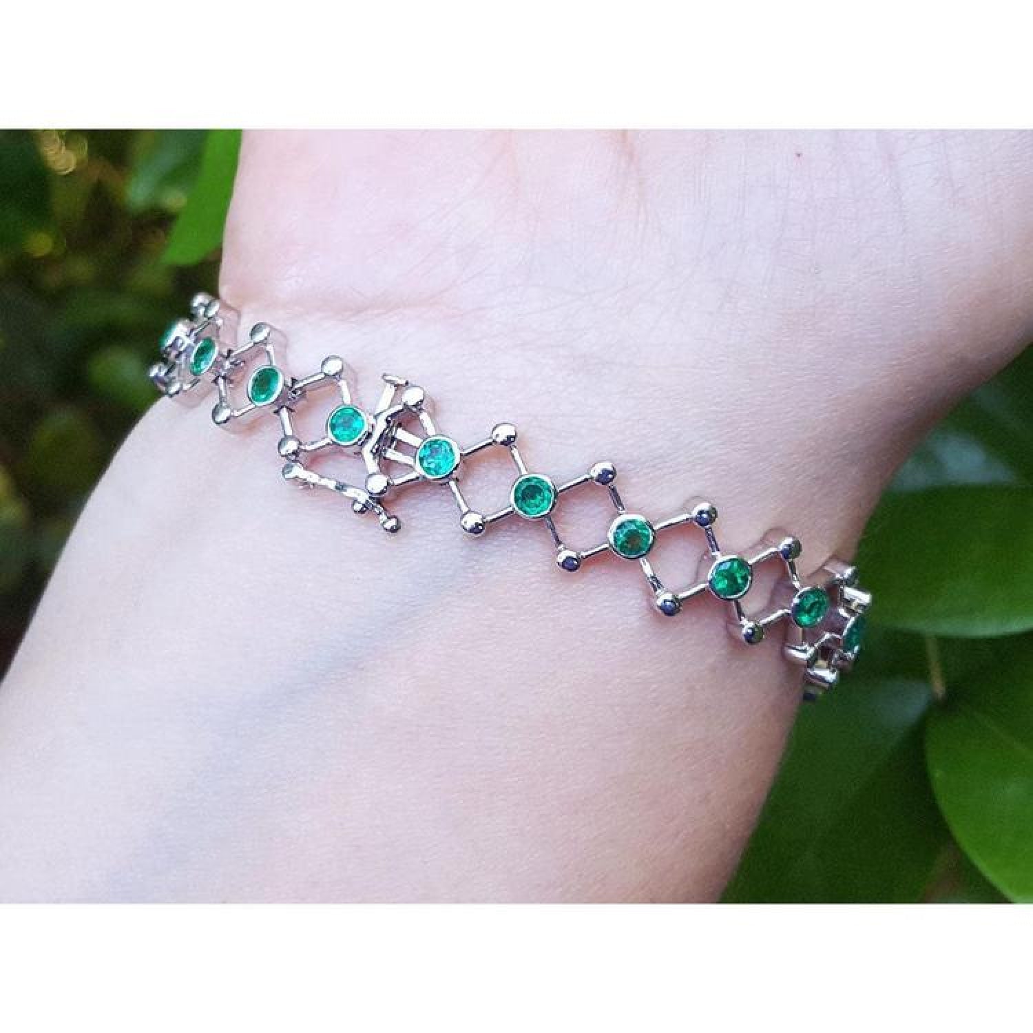 14K white gold bracelet with round Colombian emeralds bezel-set in diamond-shaped links on a wrist.