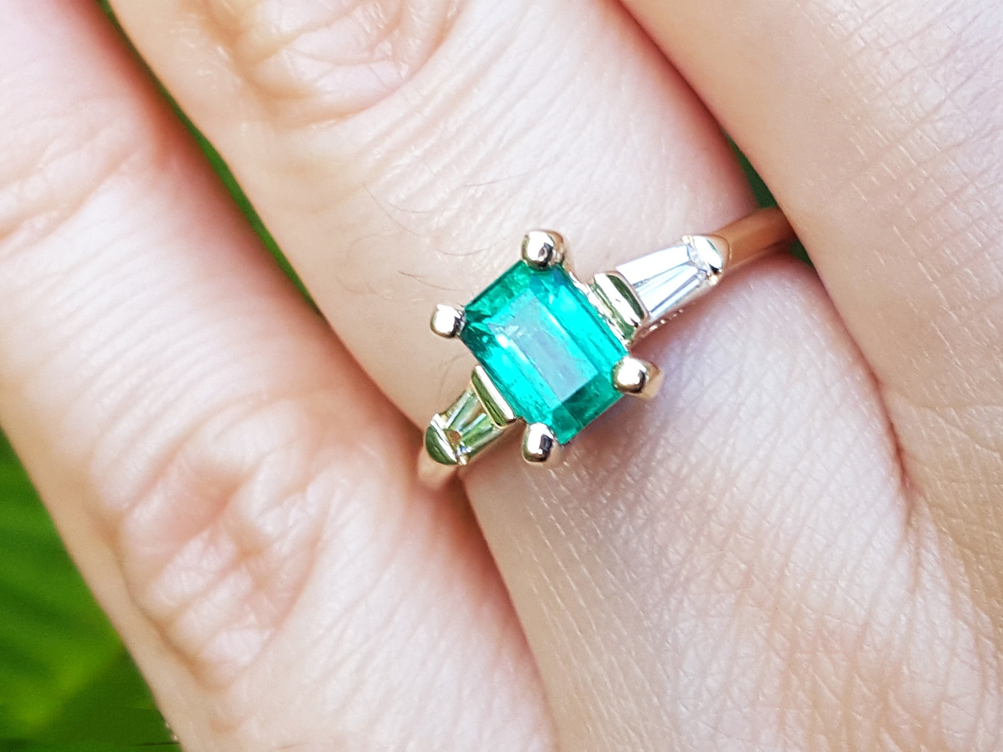 Square emerald with side baguettes gold ring on a person's finger.