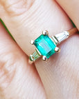 Square emerald with side baguettes gold ring on a person's finger.