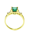 A Colombian emerald on top with side baguettes and gallery gold ring profile visibles including the band.