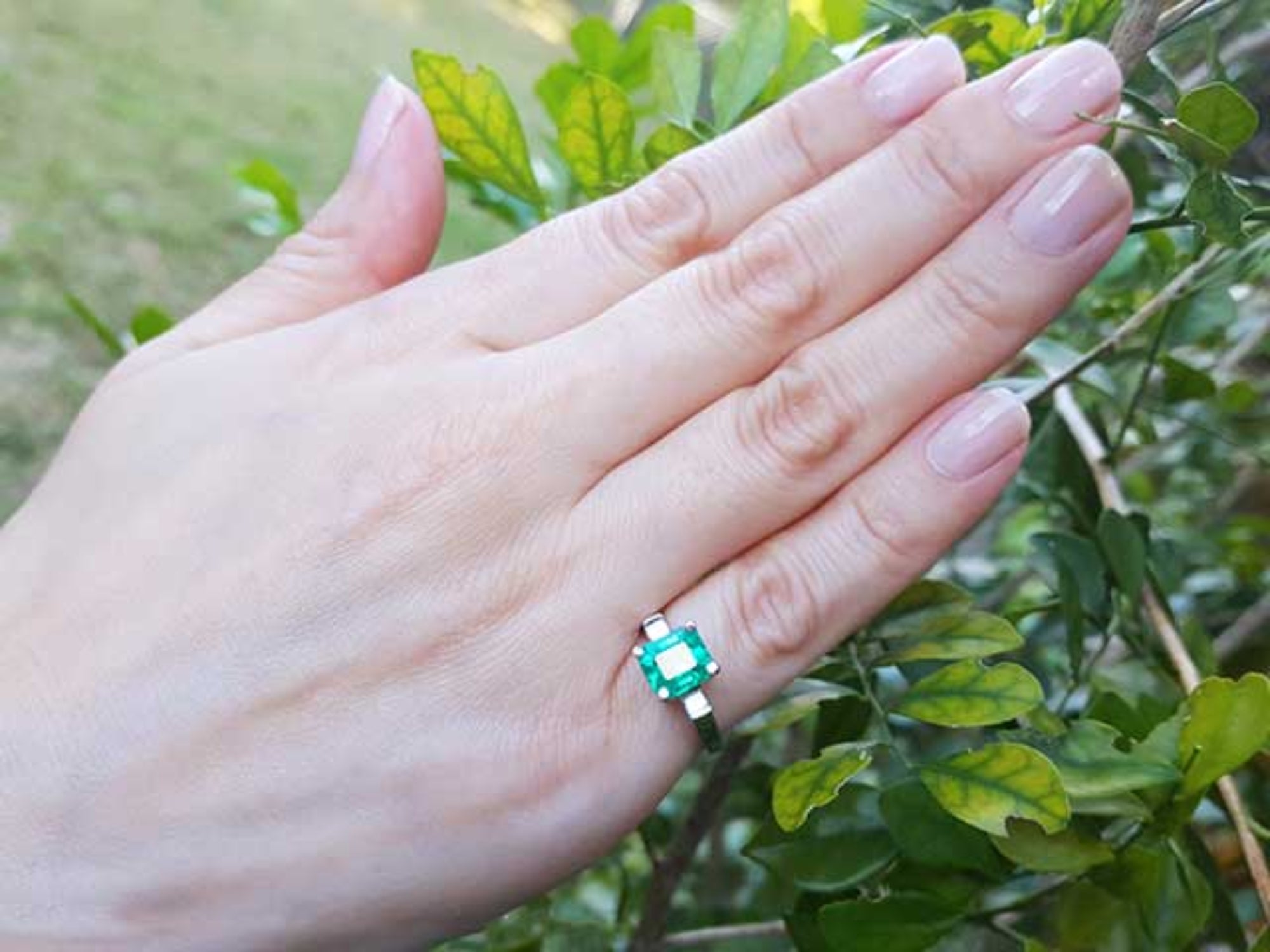 Hand wearing a natural emerald ring with a natural background.