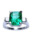 A square emerald with side princess cut diamonds ring in white gold, topside view.