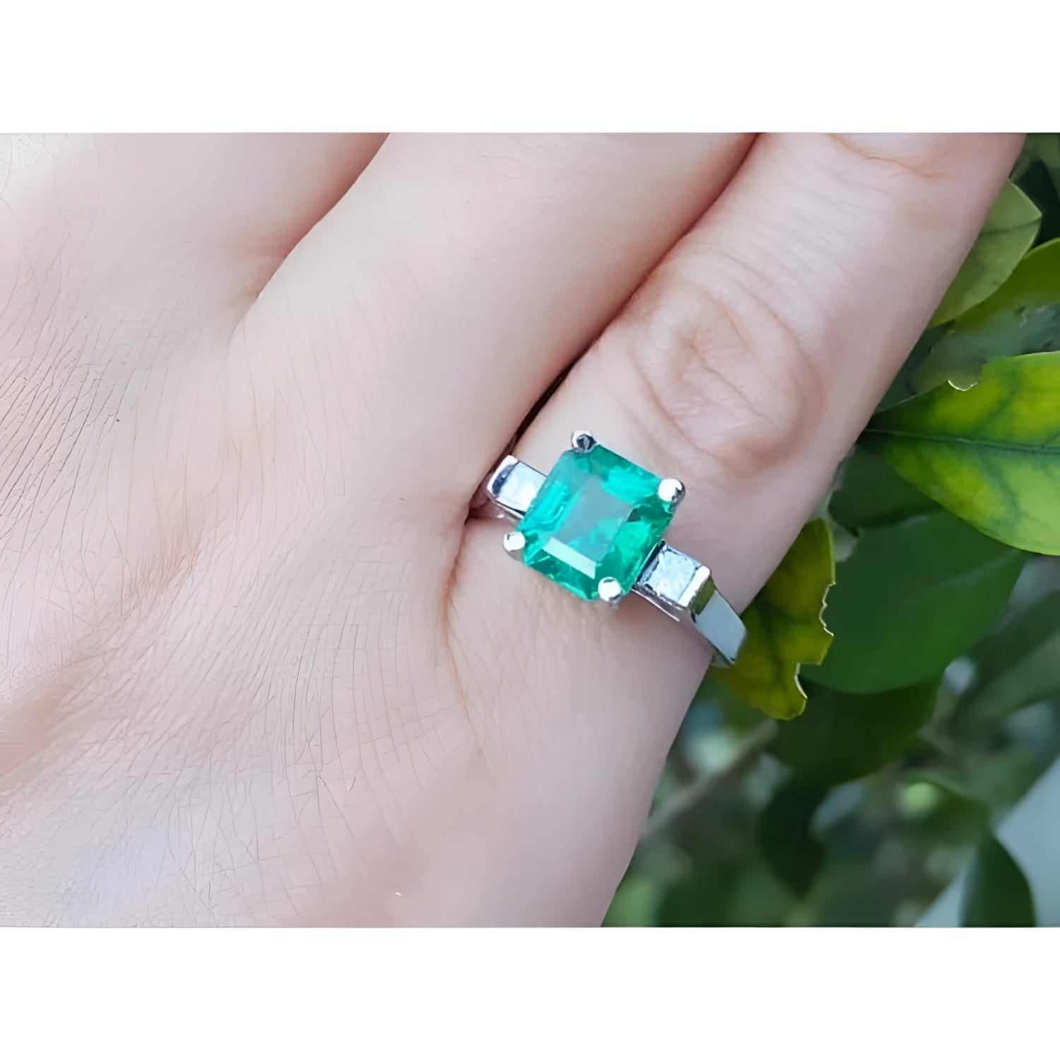 A GIA certified natural colombian emerald ring with side princess cut diamonds in 14k white gold on a finger.