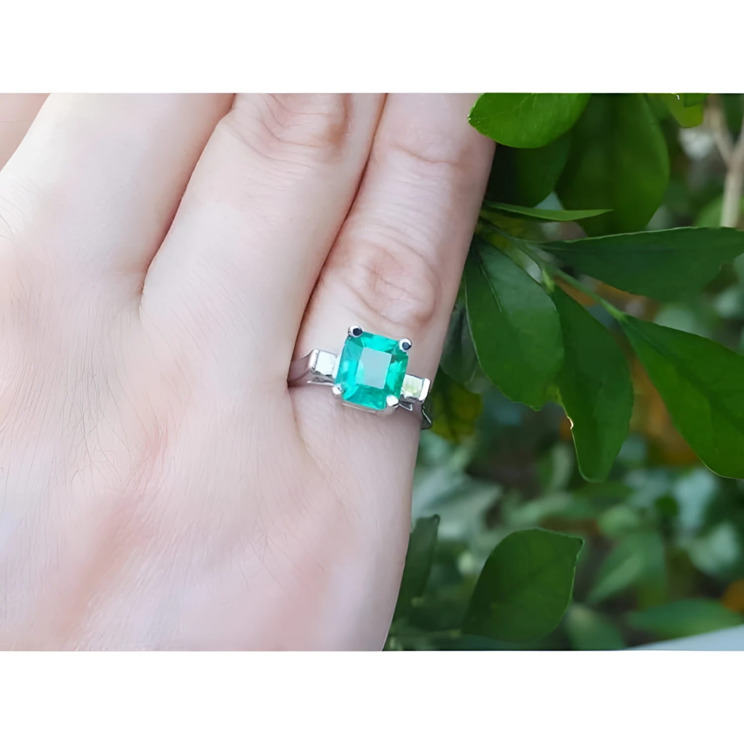 1.56 ct. emerald ring with princess-cut side diamonds set in 14K white gold on a hand.