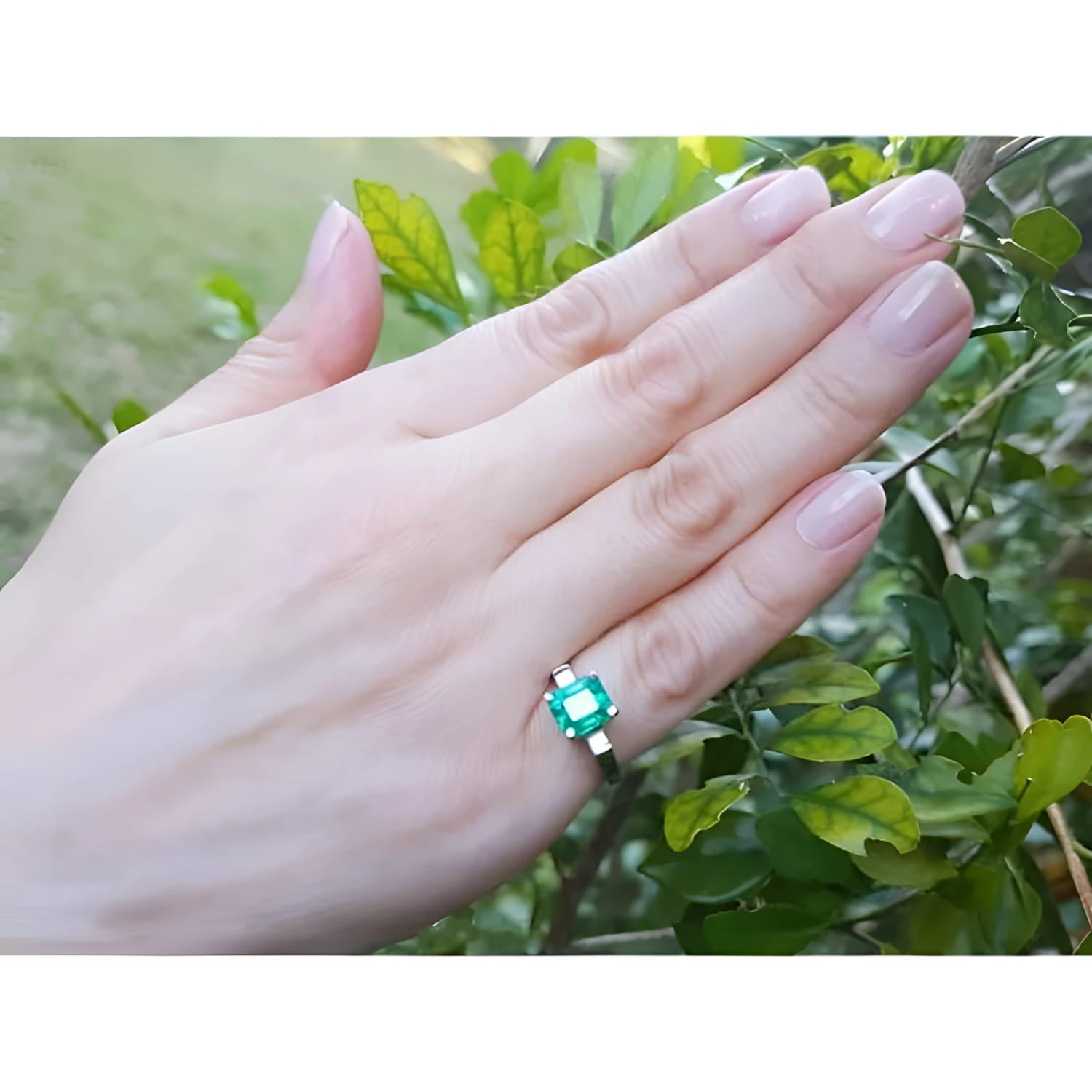 1.56 ct. emerald ring with princess-cut side diamonds in 14K white gold on a hand.