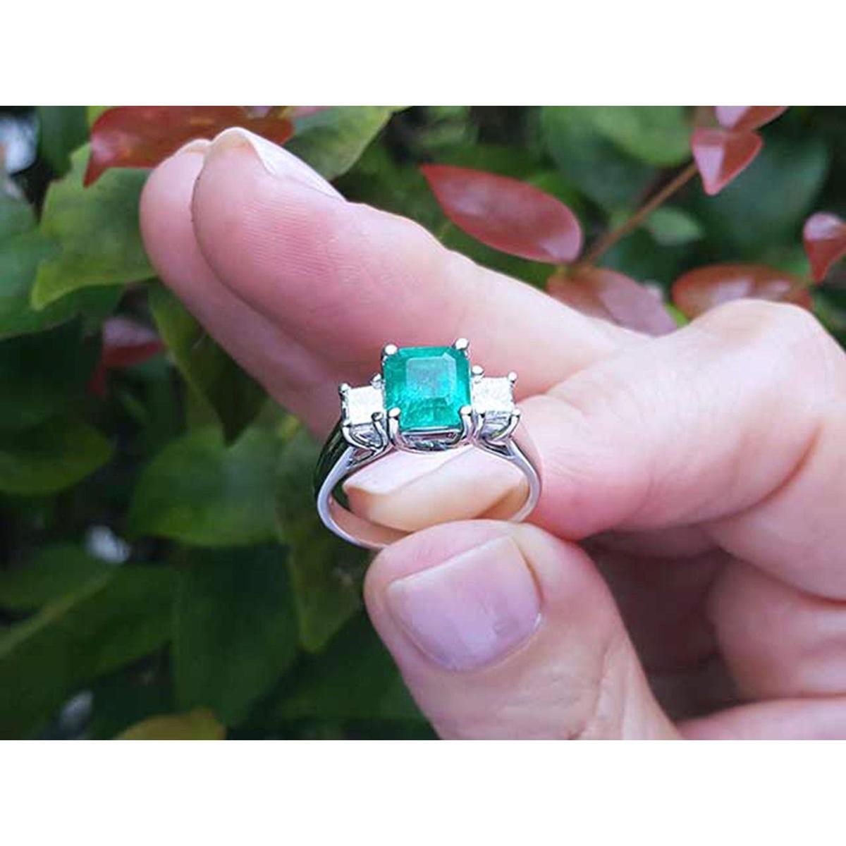Natural Colombian emerald rings held between fingers against a blurred natural background.
