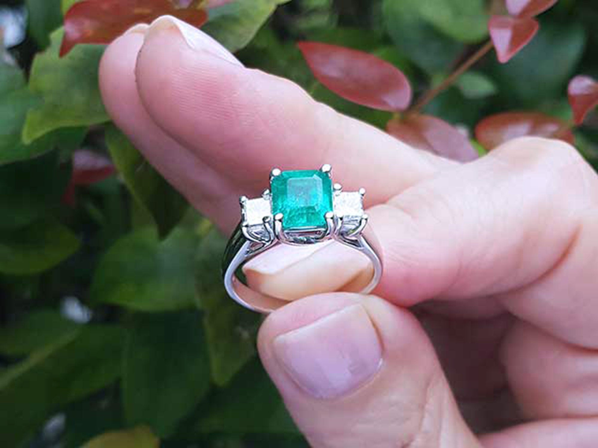 Natural Colombian emerald rings held between fingers against a blurred natural background.