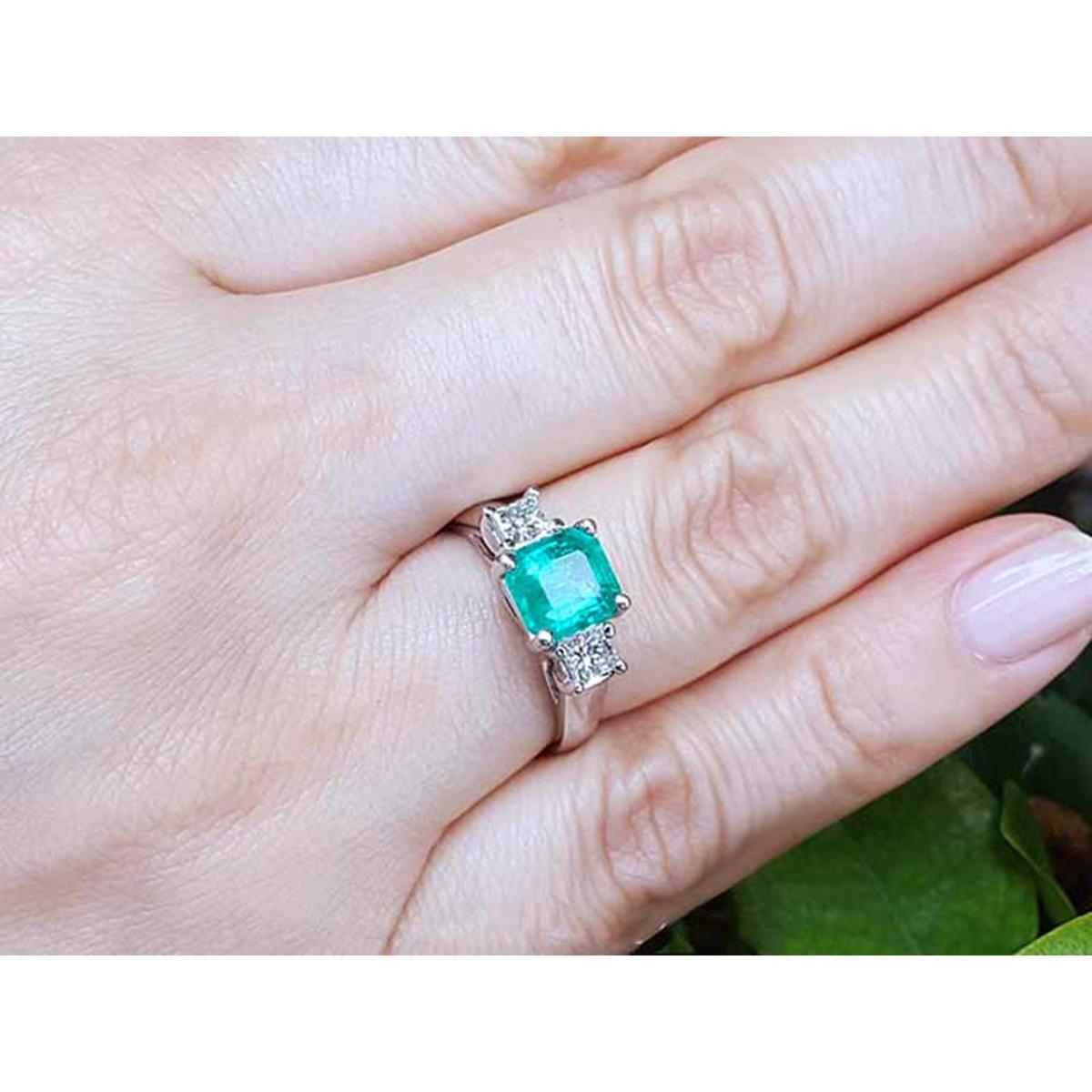 Emerald ring with diamond accents on a hand against a natural background.
