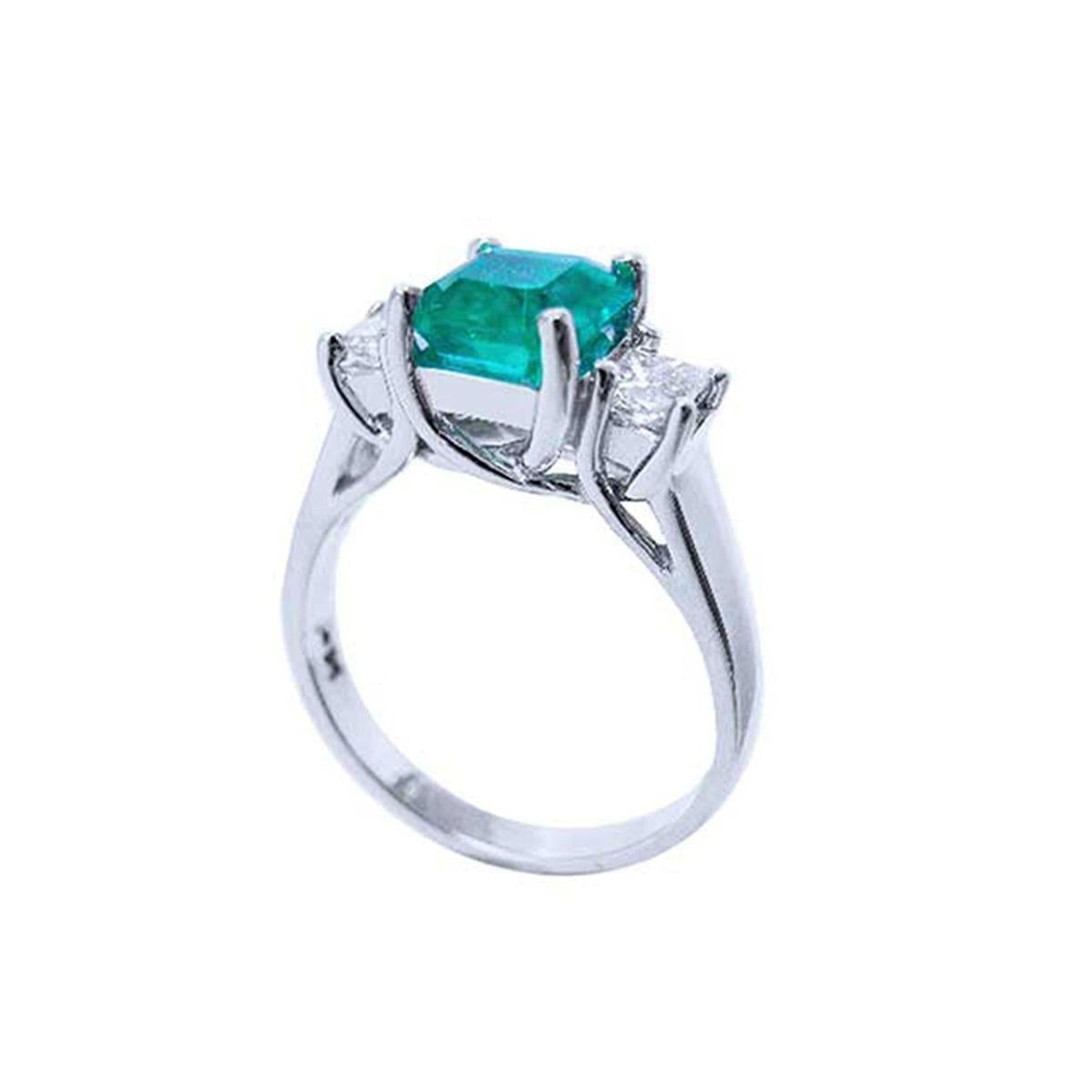 An emerald engagement ring with princess cut side diamonds on its half side profile, displaying the top and gallery. 
