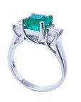 An emerald engagement ring with princess cut side diamonds on its half side profile, displaying the top and gallery. 