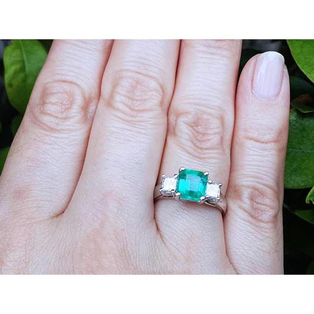 Square emerald-cut colombian emerald ring three stone with side princess cut natural diamonds on a finger.