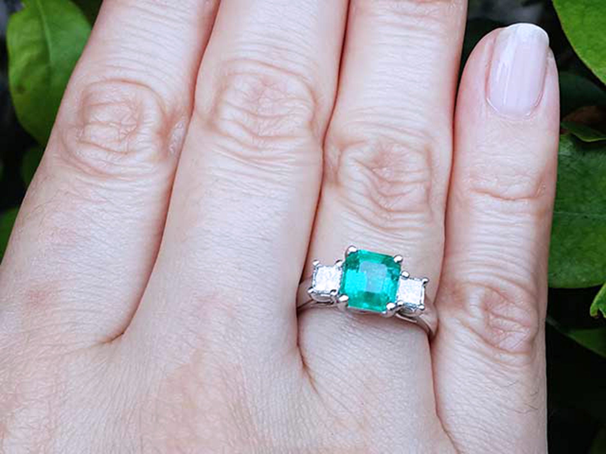 Emerald ring on a finger with a natural background.