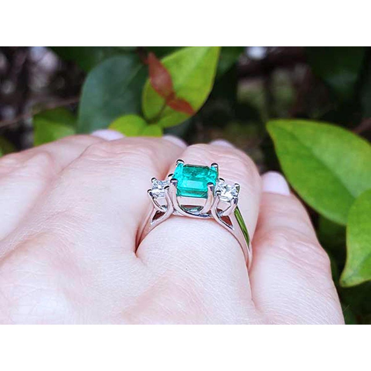 Natural emerald rings on a hand with a blurred green leafy background.