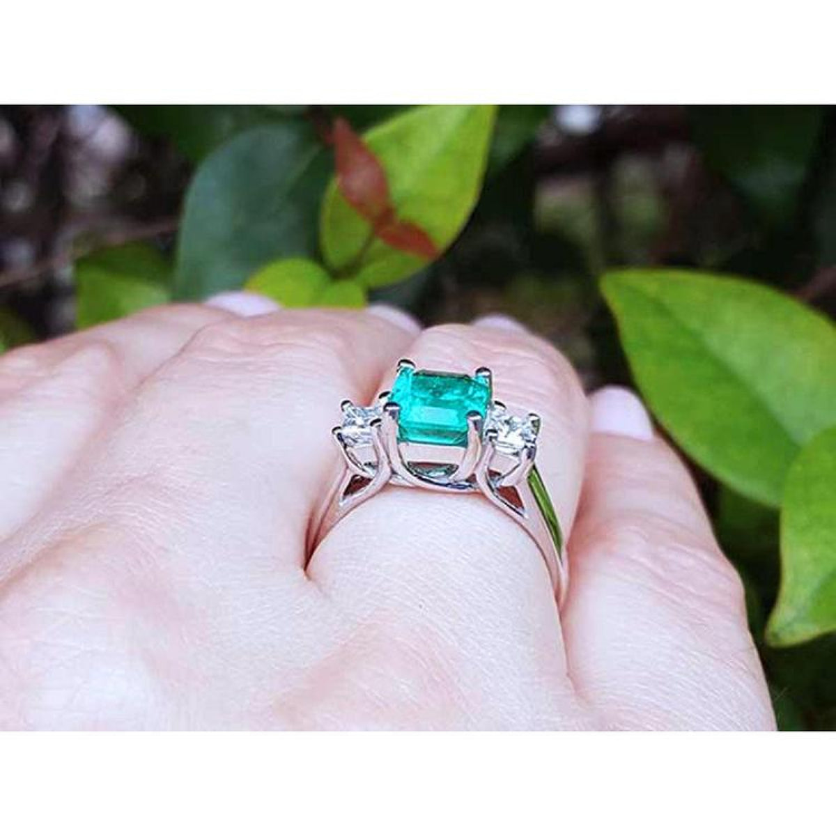 1.62 carat emerald engagement ring with princess cut diamonds in 14k white gold on a hand.