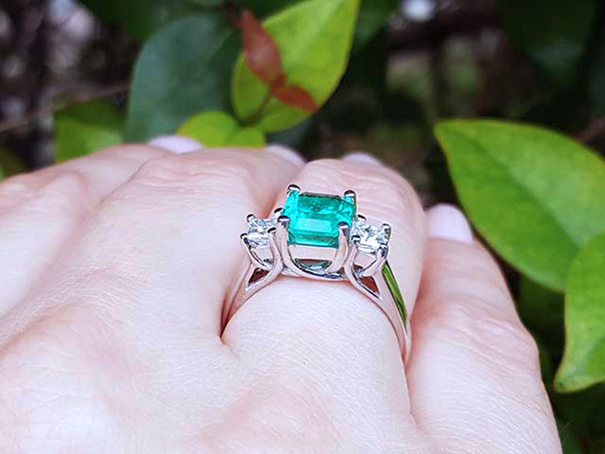 Natural emerald rings on a hand with a blurred green leafy background.