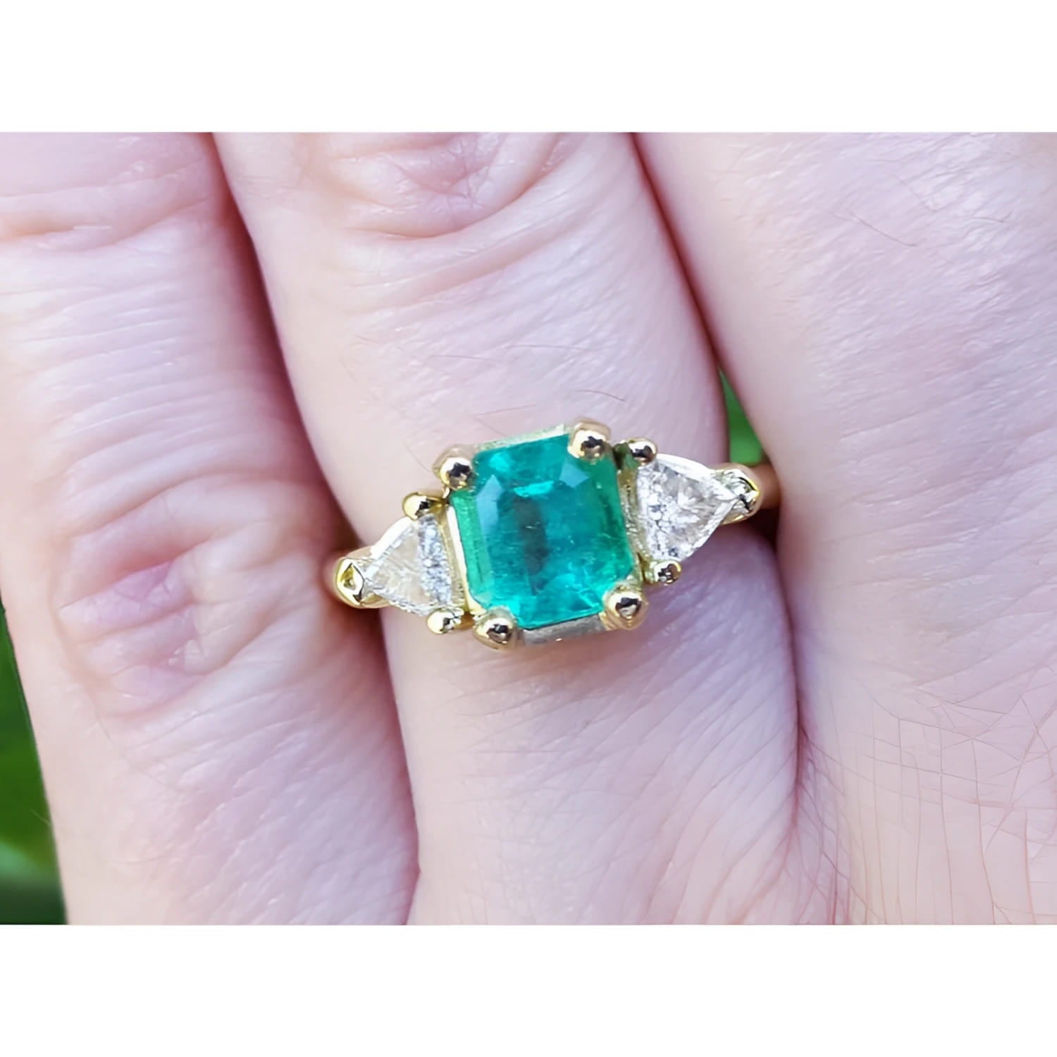 A 18k yellow gold colombian emerald ring with side trillion cut natural diamonds on a finger.