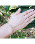A woman's hand wearing a gold bracelet with a colombian emerald against a natural background.