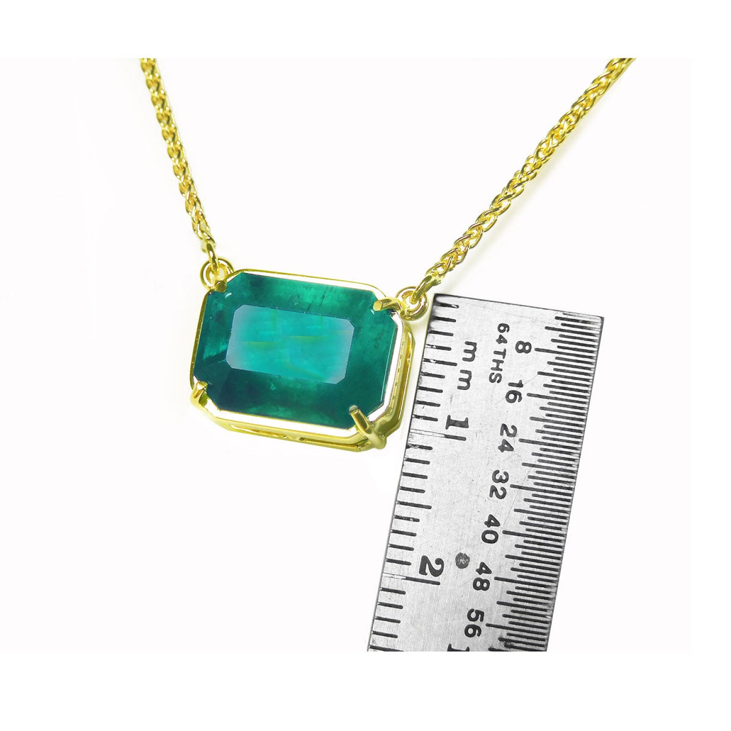 Emerald-cut Colombian emerald solitaire necklace in 18K yellow gold, shown with a ruler for scale.
