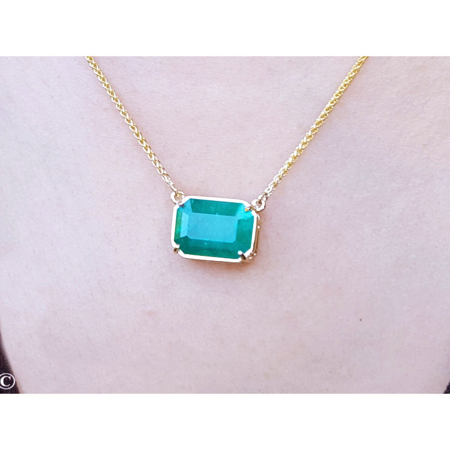 Emerald-cut Colombian emerald solitaire necklace in 18K yellow gold, shown worn on a person's neck.