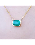 Emerald-cut Colombian emerald solitaire necklace in 18K yellow gold, shown worn on a person's neck.