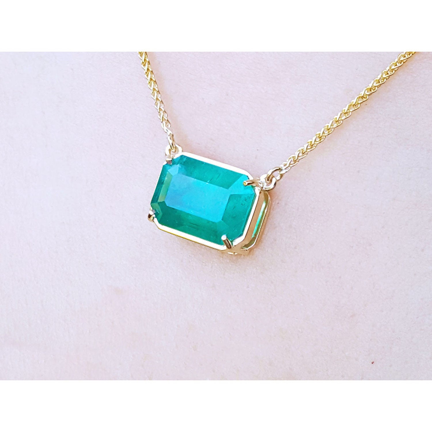 Emerald-cut Colombian emerald solitaire necklace in 18K yellow gold, displayed on a light skin-toned surface.