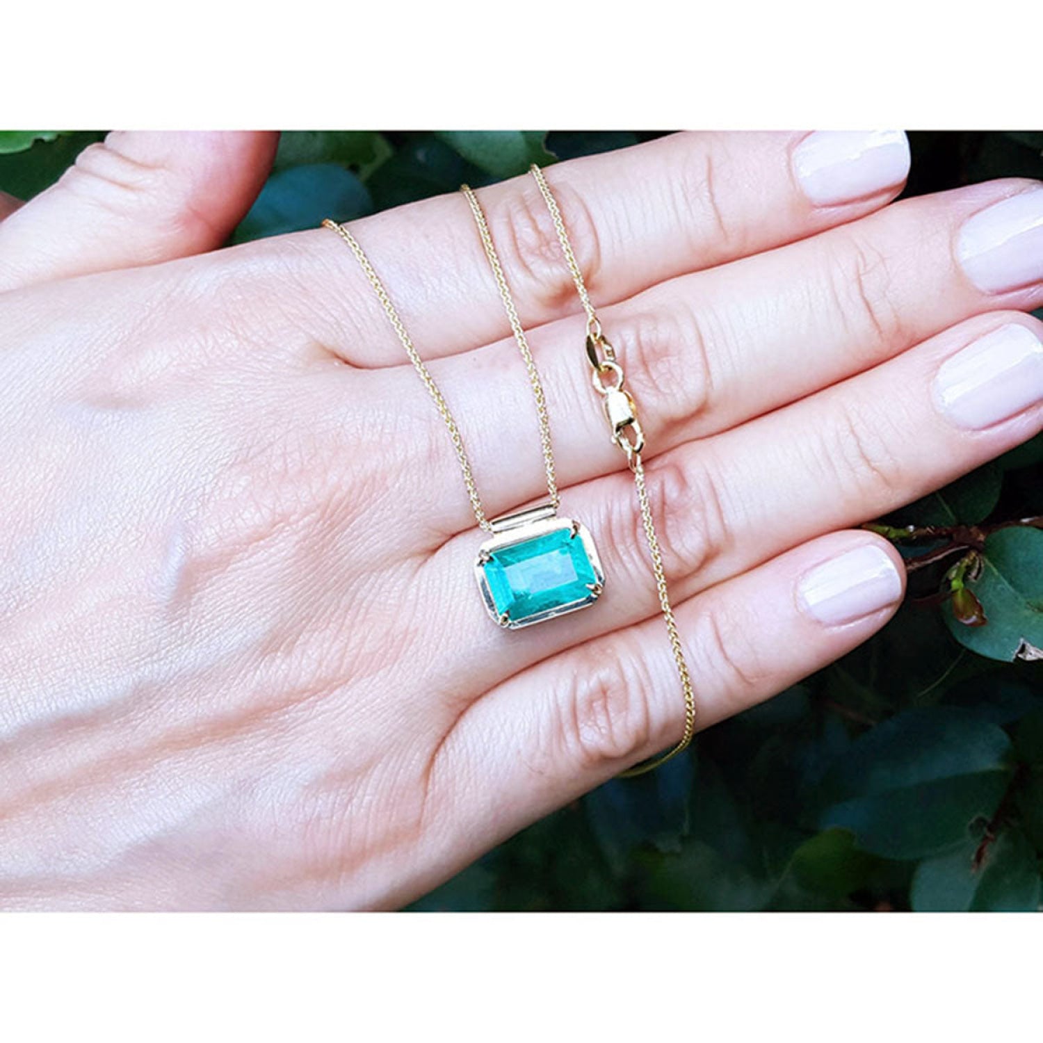 Deep green emerald solitaire necklace in 18K yellow gold, held in a hand.