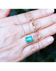 Deep green emerald solitaire necklace in 18K yellow gold, held in a hand.