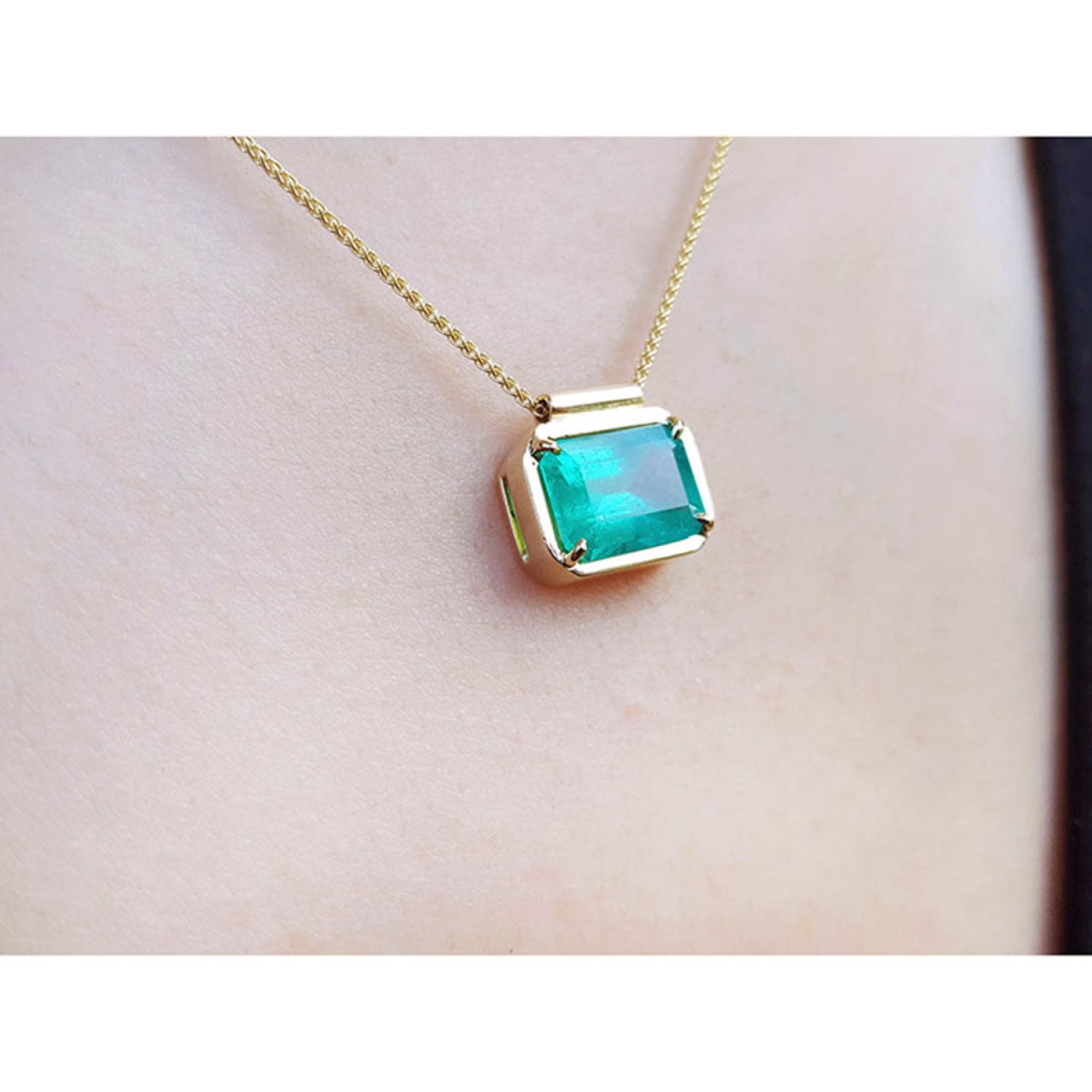 18K yellow gold necklace with a vibrant deep green emerald solitaire in an east-west setting.