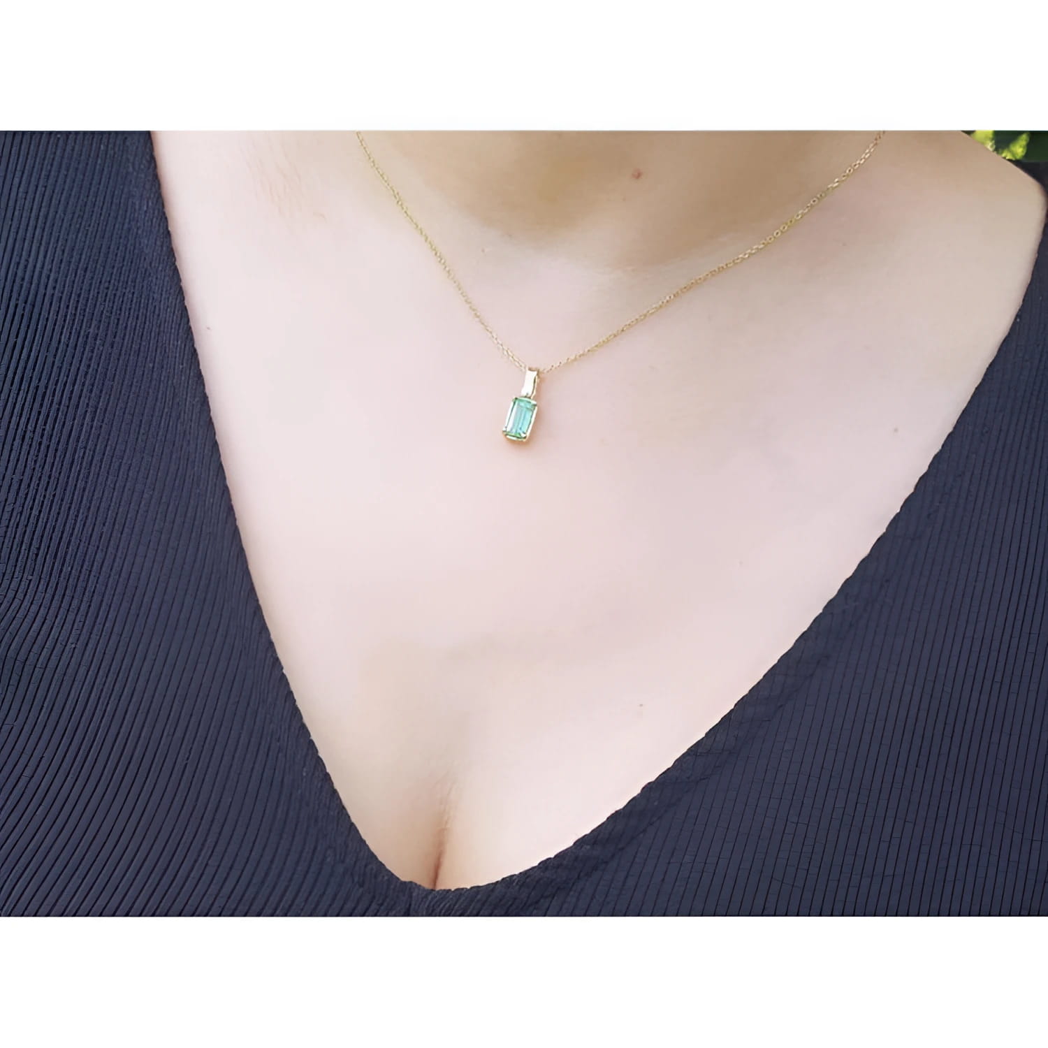 Emerald solitaire pendant necklace in 14K yellow gold on a woman's chest.