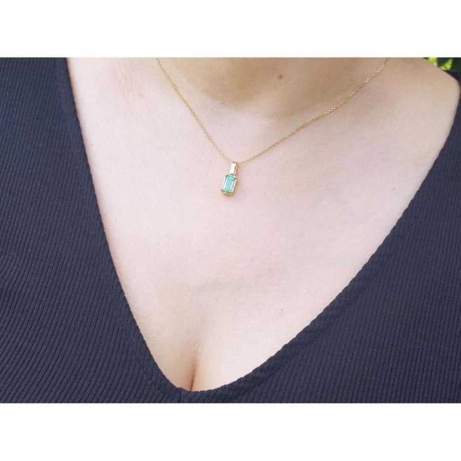 Emerald solitaire pendant necklace in 14K yellow gold on a woman's chest.
