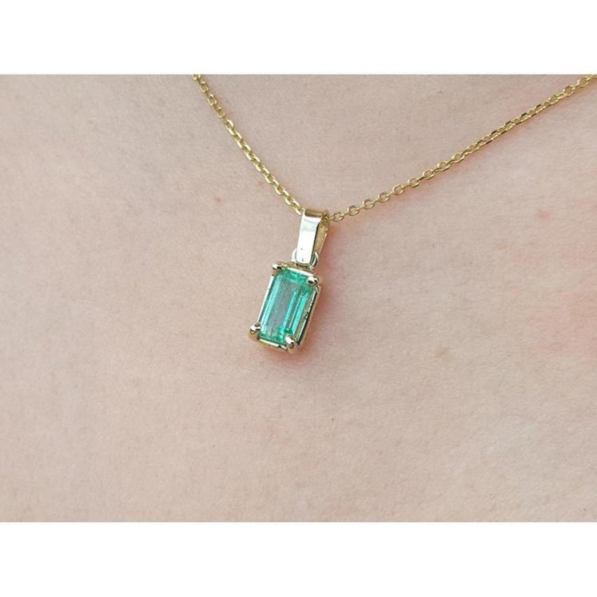 1.31 ct. emerald solitaire pendant in 14K yellow gold on a delicate chain, worn on a person.