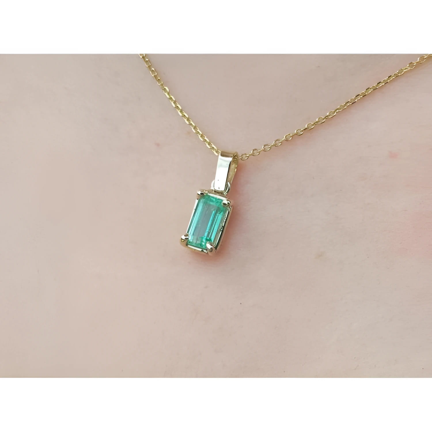 1.31 ct. emerald solitaire pendant in 14K yellow gold on a delicate chain, worn on a person.