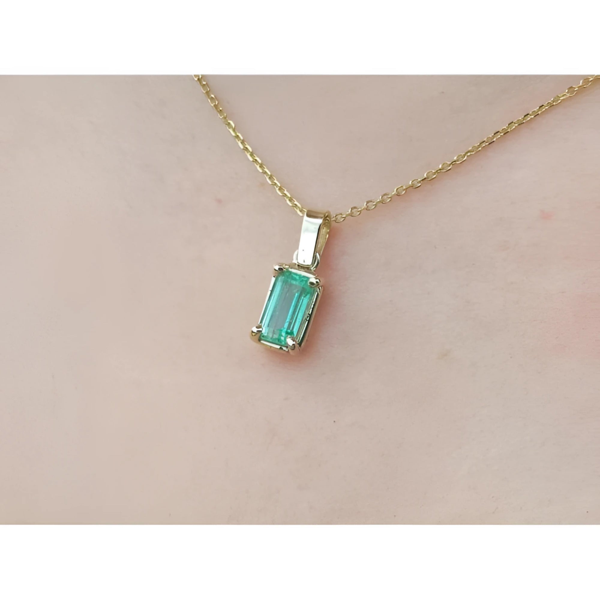 1.31 ct. emerald solitaire pendant in 14K yellow gold on a delicate chain, worn on a person.