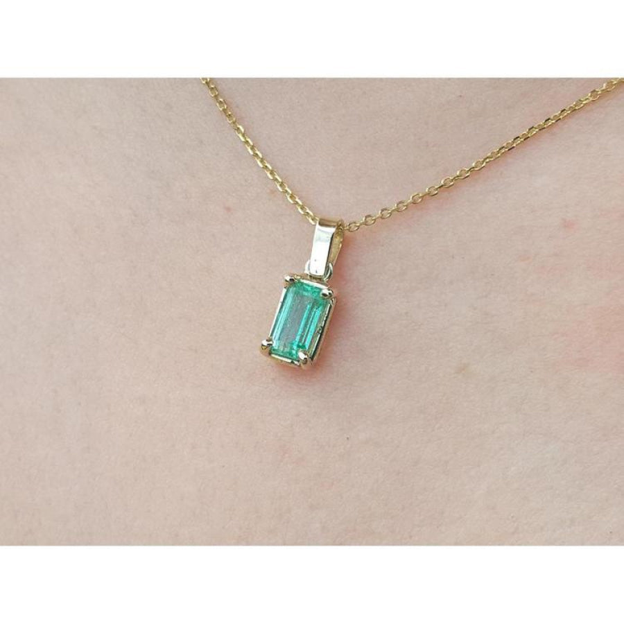 1.31 ct. emerald solitaire pendant in 14K yellow gold on a delicate chain, worn on a person.
