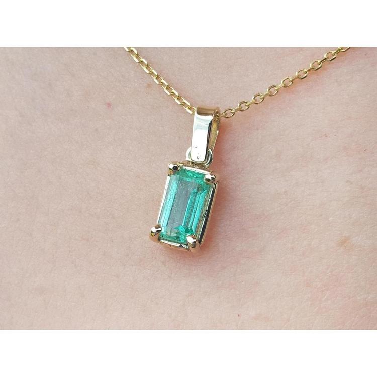 Gold necklace with a natural emerald pendant on a beige skin background