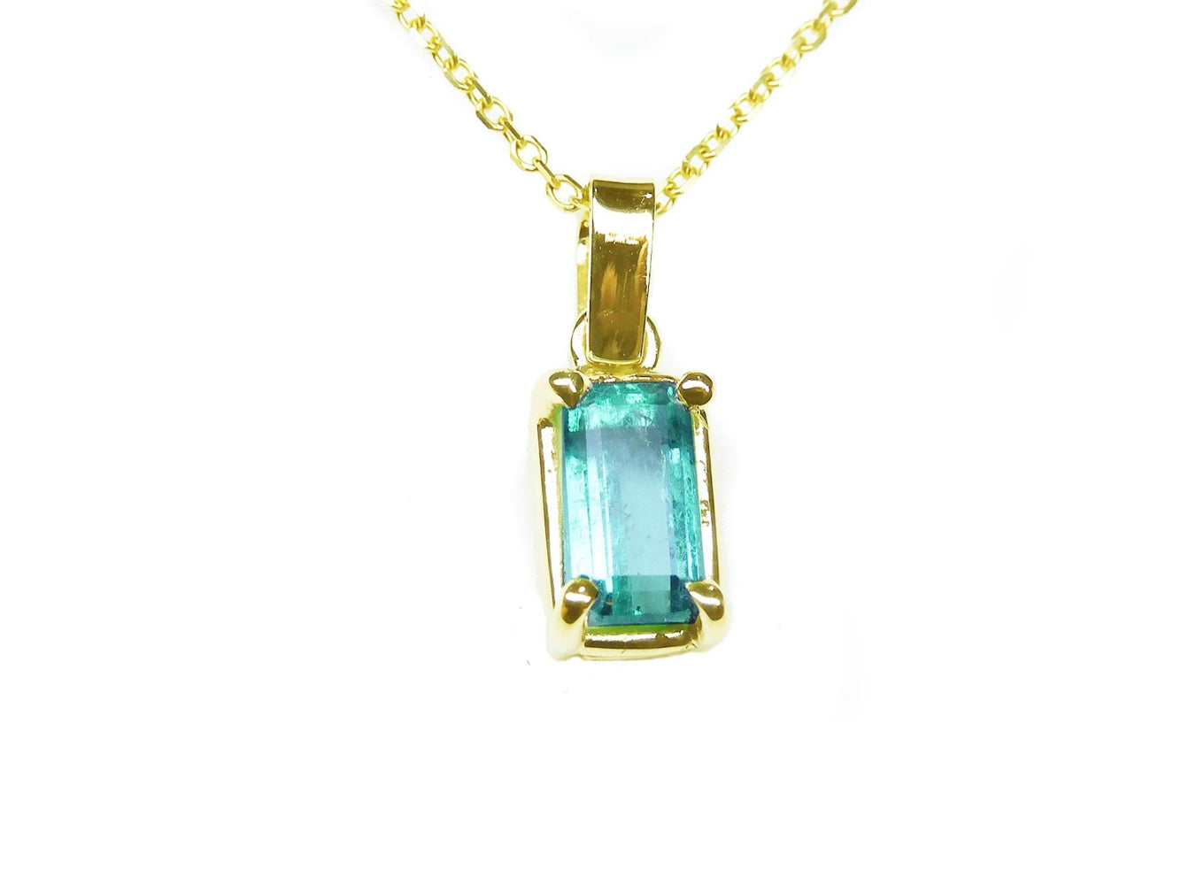 This solitaire emerald pendant displays the topside with a yellow gold frame on a chain.