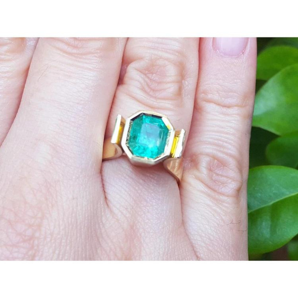 Emerald solitaire ring bezel set in 14k yellow gold on a hand.
