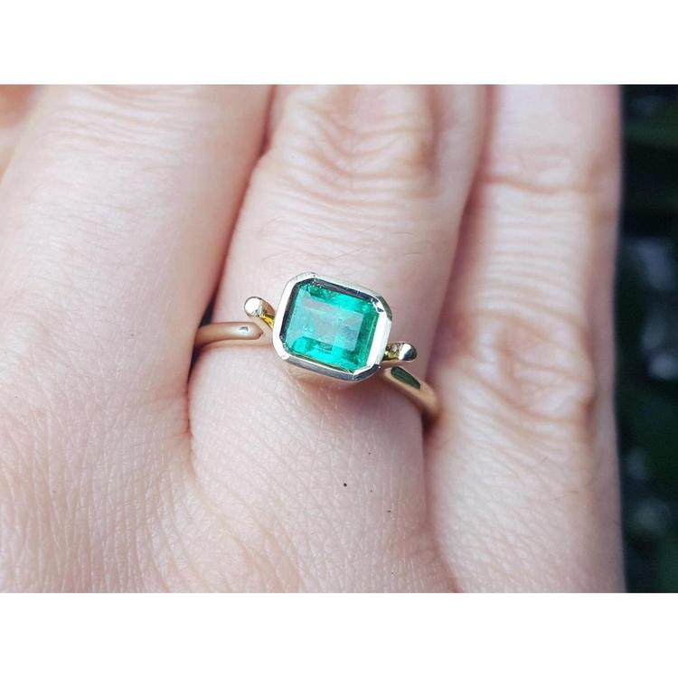 An emerald solitaire ring crafted in 14k yellow gold on a finger