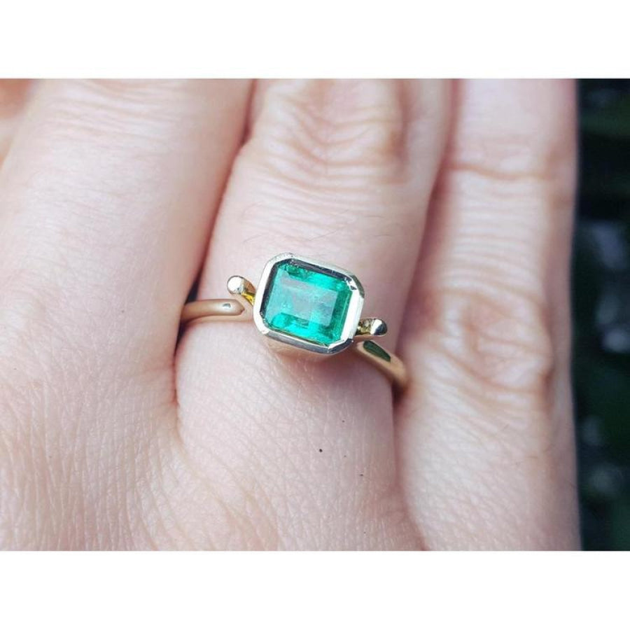 An emerald solitaire ring crafted in 14k yellow gold on a finger