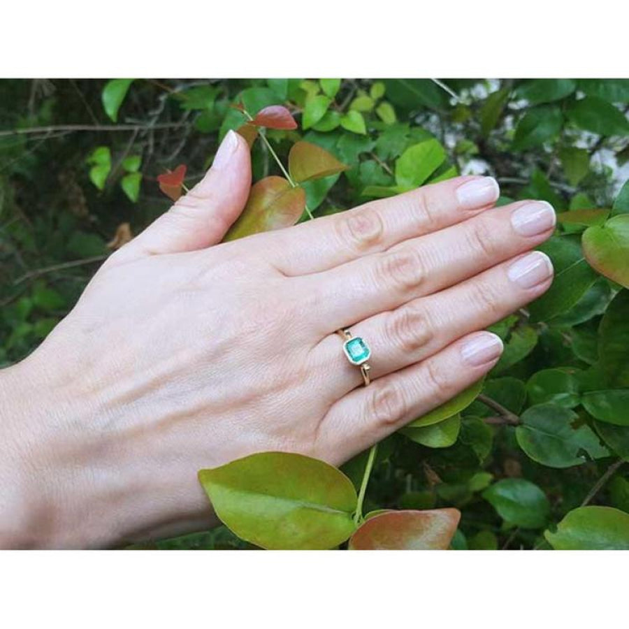 Hand wearing a 0.81 ct. medium bluish green emerald solitaire ring, bezel set in 14K yellow gold.