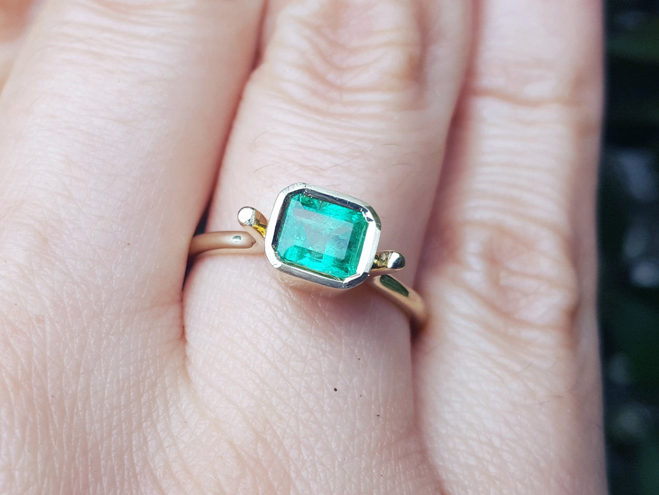 An emerald solitaire ring yellow gold on a finger