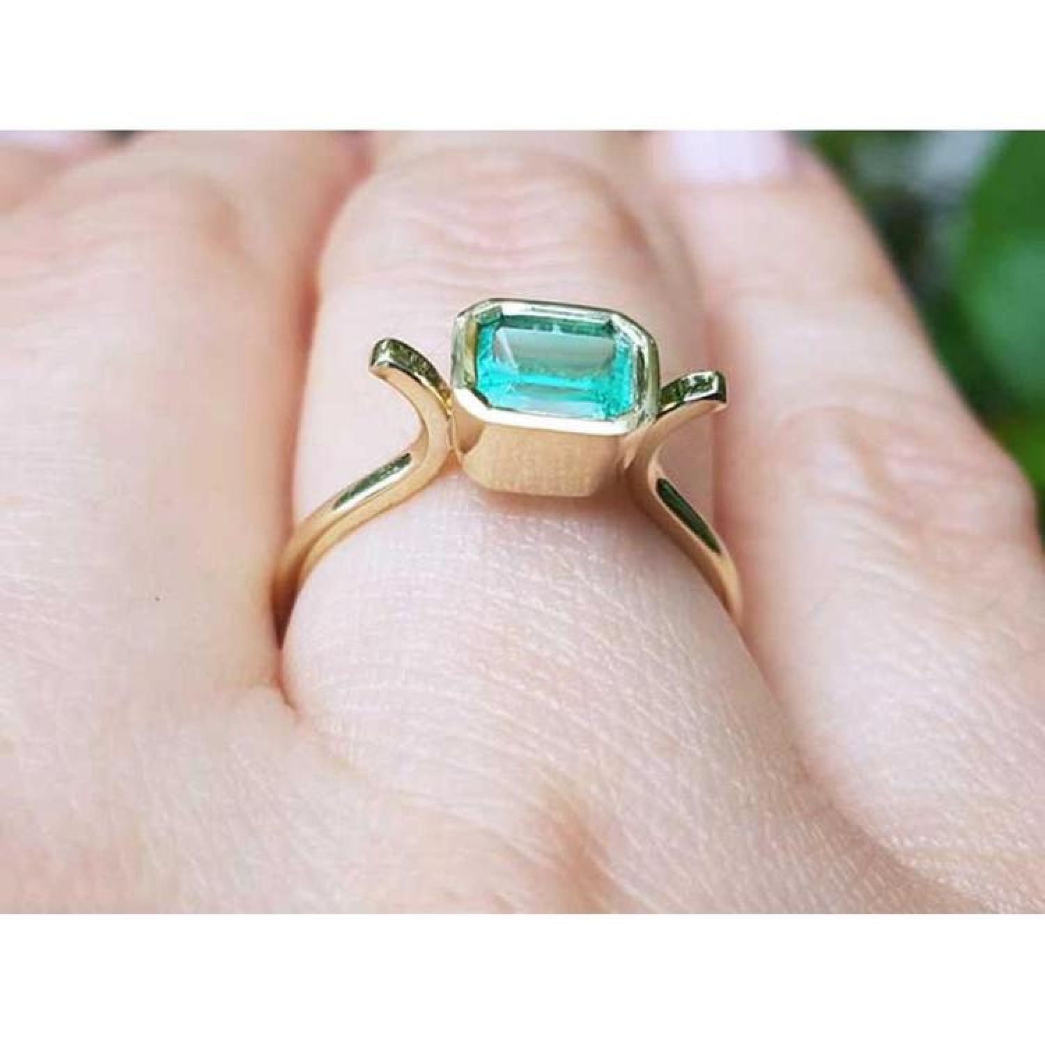 0.81 ct. emerald solitaire ring, bezel set in 14K yellow gold, worn on a finger.