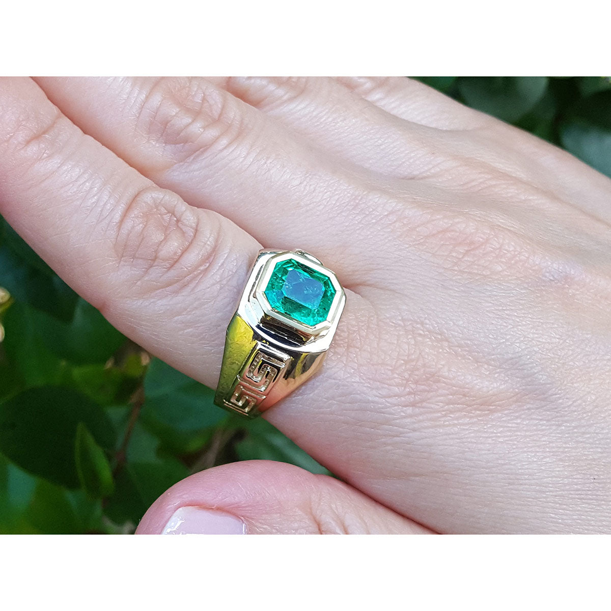 A 18k yellow gold ring with a bezel set genuine colombian emerald on a hand against a natural background.